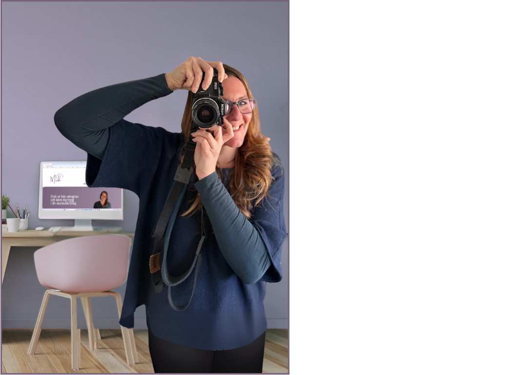 Kvinna som tar foto med en systemkamera vänd framåt, i bakgrunden syns ett skrivbord med en dator